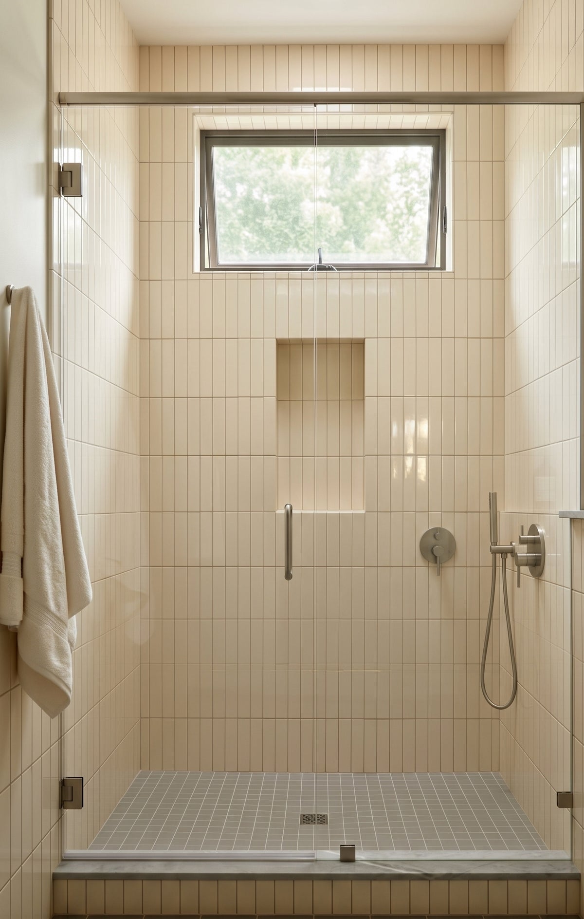 A modern walk-in shower features vertical cream subway tiles, a built-in shower niche, and a sleek glass door.