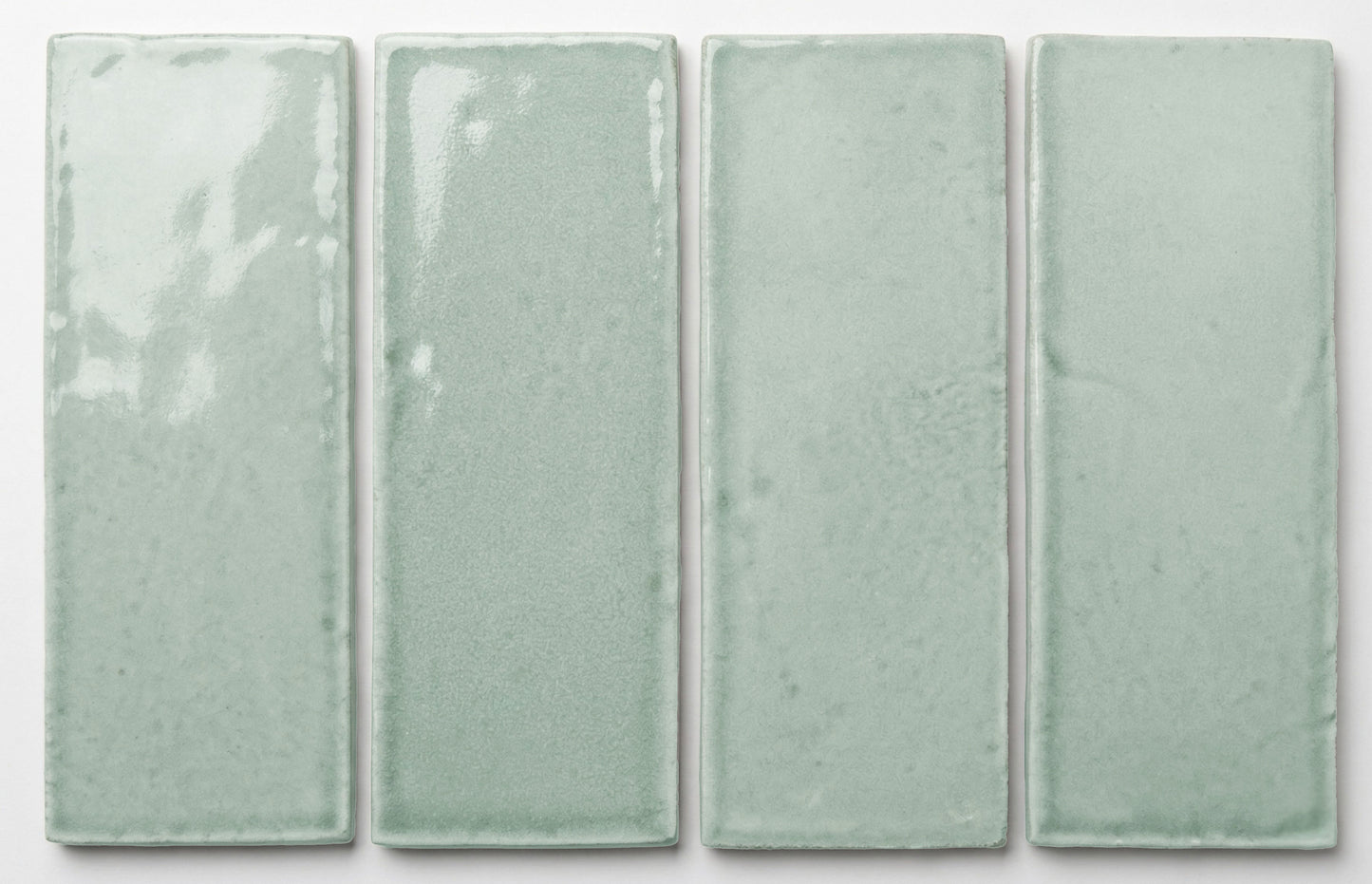 Four rectangular 2x6 light seafoam green glossy tiles by Clay Imports, showing subtle texture variations.