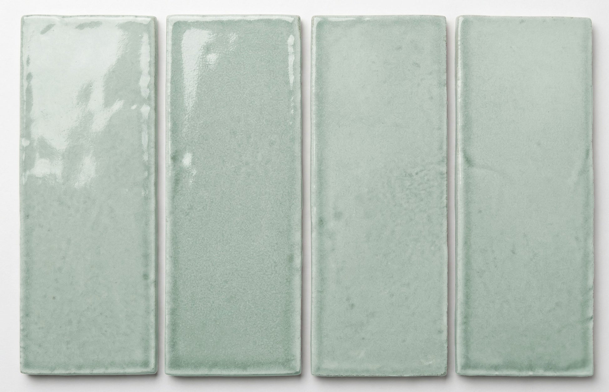 Four rectangular 2x6 light seafoam green glossy tiles by Clay Imports, showing subtle texture variations.