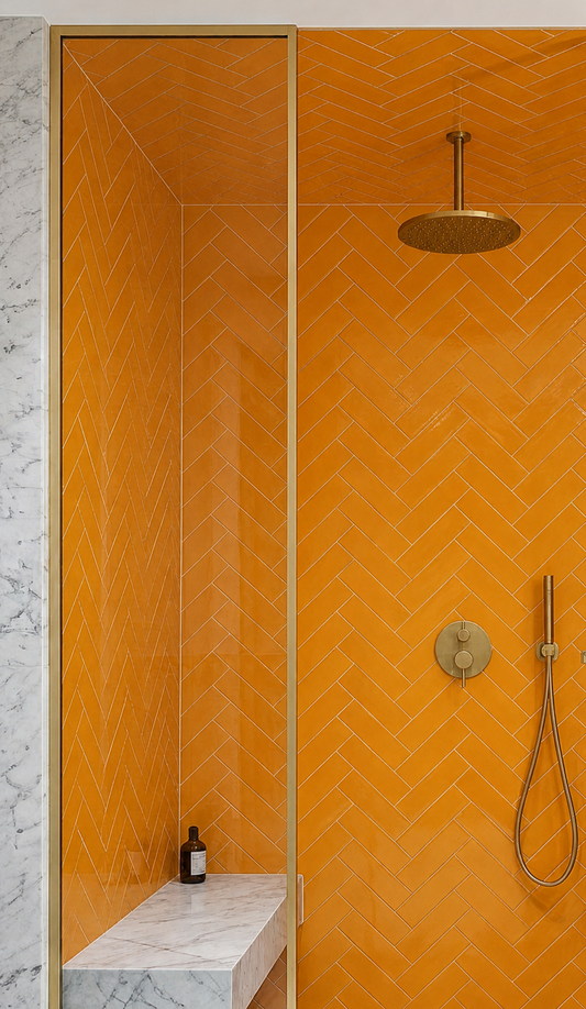 Marigold solid tile by Clay Imports in a glossy herringbone pattern, installed in a modern shower with gold fixtures and a marble bench.
