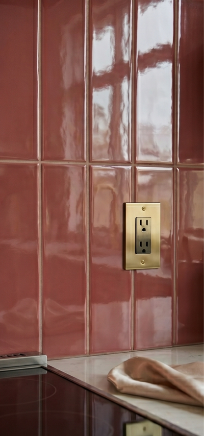 Burgundy Gloss 2x12 Solid Tile by Clay Imports forming a kitchen backsplash with a brass electrical outlet.