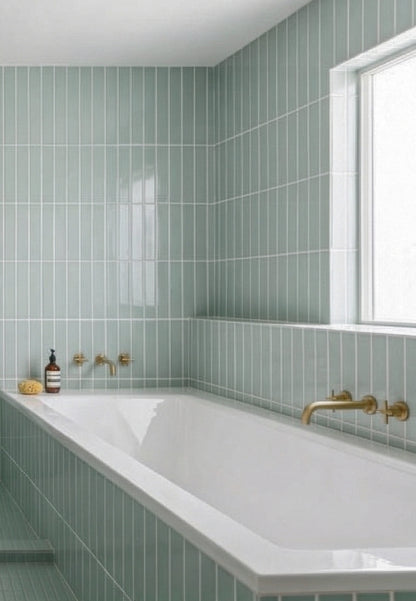 Glossy mint green vertical 2x12 tile by Clay Imports on bathroom walls with a white tub and brass fixtures.