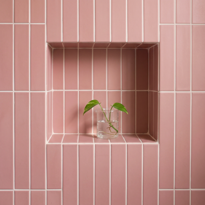 Pink rectangular wall tiles arranged in a recessed niche with a small glass vase and green plant on the shelf, shown against a white background.