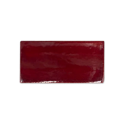 Oxblood red glossy tile sample from Clay Imports, rectangular with a rich, reflective finish and slightly textured edges.