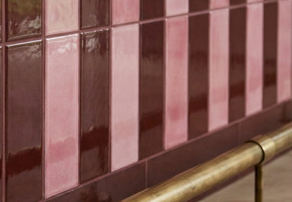 Glazed ceramic tiles by Clay Imports in alternating dark brown and pink vertical stripes with a brass rail.