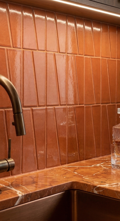 Brandy-colored clay tiles by Clay Imports with glossy, angled surfaces arranged vertically above a marble countertop.