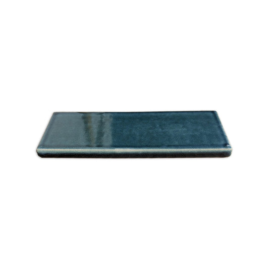Botanical Teal subway solid tile trim with glazed edges by Clay Imports, lying flat from an angled view.