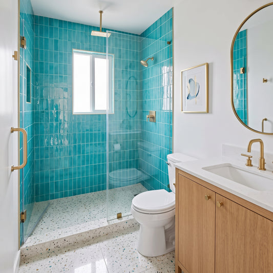 A modern bathroom featuring a walk-in shower with bright turquoise blue mosaic tile walls and a glass door, paired with a white toilet, light wood vanity cabinets, a white countertop, and a round gold-framed mirror on a white wall.