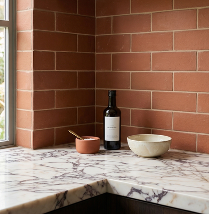 Rectangular Umber Cotto tiles by Clay Imports in a kitchen backsplash with light grout and a marble countertop.