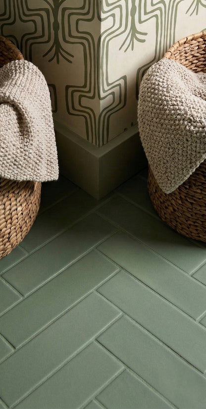 Cilantro green 2x8 clay tiles by Clay Imports, laid in herringbone on floor beside patterned wallpaper and woven baskets with blankets.