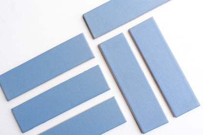 Blue matte subway tiles by Clay Imports arranged in a herringbone pattern on a white background.