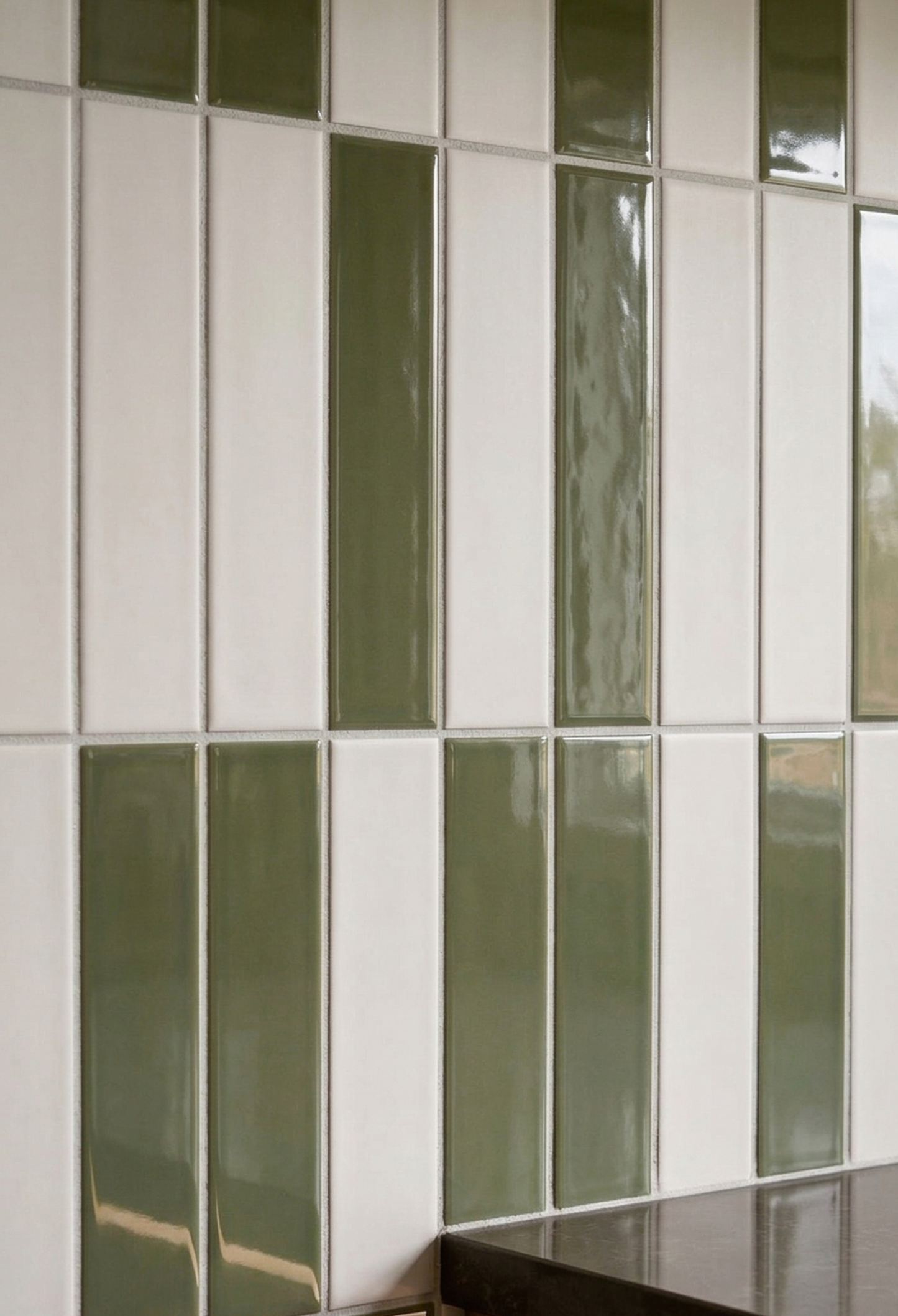 Green and white rectangular solid tiles by Clay Imports with a matte finish, arranged in alternating vertical stripes above a dark countertop.