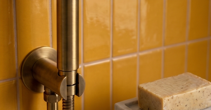 Glossy yellow clay tiles by Clay Imports, arranged on a wall next to a brass shower fixture and natural soap.