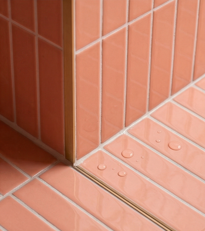 Glossy coral 2x8 solid tiles by Clay Imports with white grout, installed on a wall and wet floor corner with a gold trim.