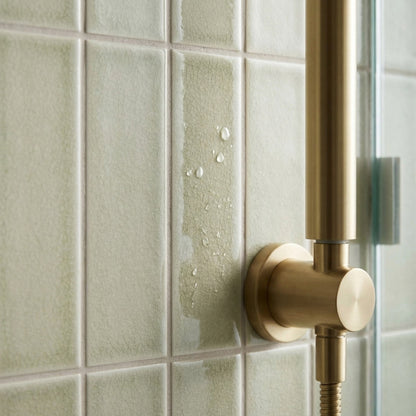 Yucca Crackle Gloss 2x8 tile by Clay Imports, light green with crackle texture and water droplets, next to a brass shower fixture.