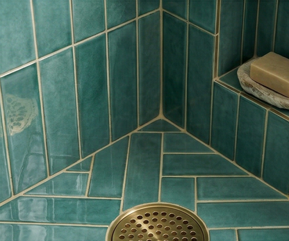Grotto Green clay tiles by Clay Imports in a geometric and chevron pattern within a shower corner, with a brass drain and soap.