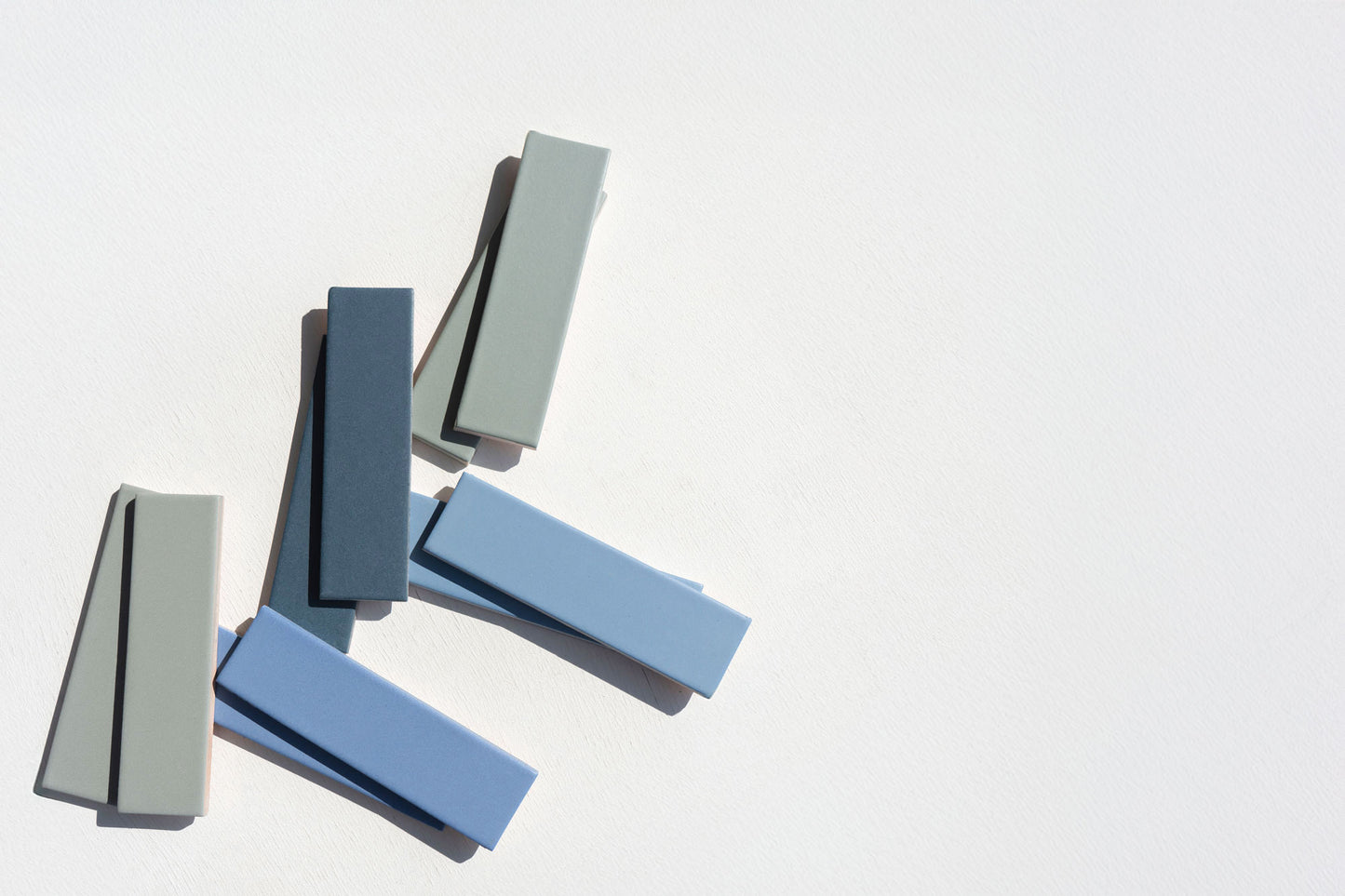 Blue Agate 2x8 clay tiles by Clay Imports, arranged with dark blue and gray rectangular tiles, casting shadows on a white textured background.