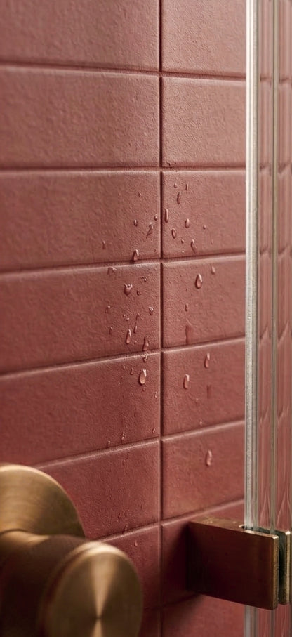Lava Rock Matte 2x12 solid tile by Clay Imports, featuring a textured surface with water droplets and a brass shower fitting.