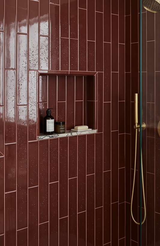 Shower area with burgundy tiles, a niche shelf, and bathroom products.