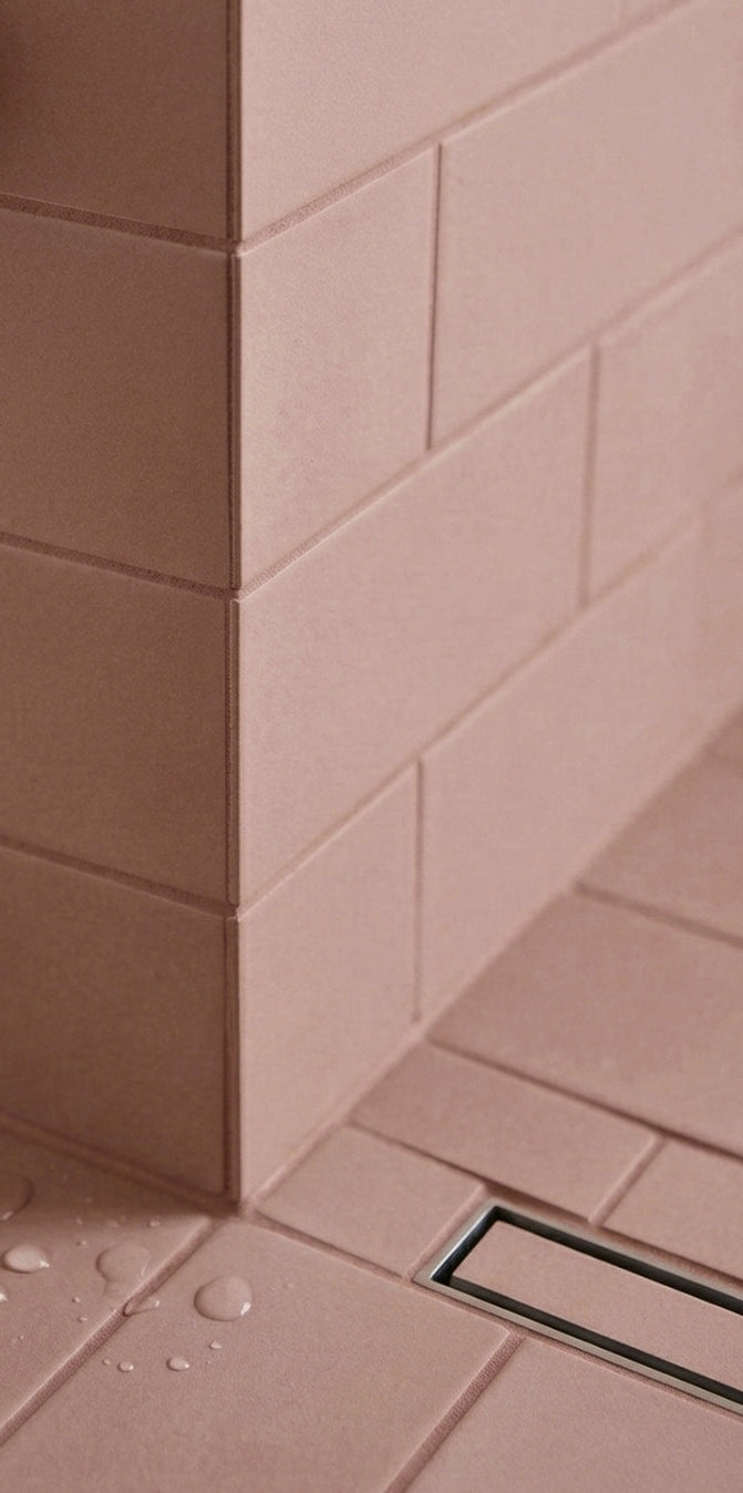 Rosewater Matte Solid Tile by Clay Imports installed in a shower corner, showing its textured surface, a linear drain, and water droplets.