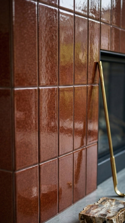 Tamarindo Gloss solid tiles by Clay Imports, a reddish-brown textured finish on a fireplace surround, with a brass tool and petrified wood.