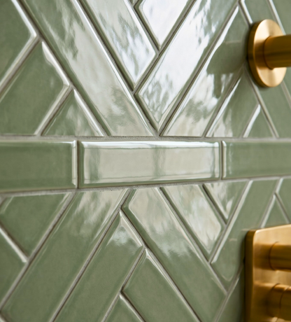 Glossy green 2x8 solid tile by Clay Imports in a herringbone and horizontal stripe pattern, with brass fixtures.