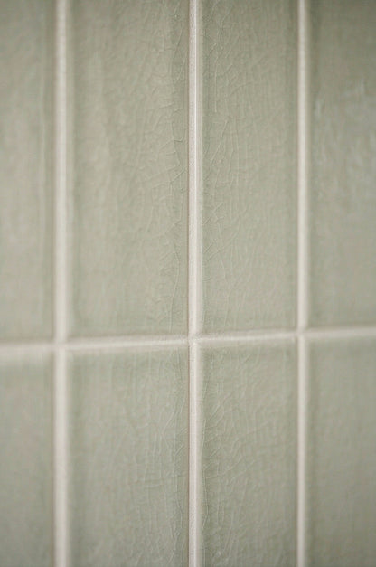 Close-up of sage green crackle gloss rectangular tiles by Clay Imports, featuring white grout and visible texture.