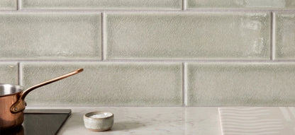 Light sage green rectangular Yucca Crackle Gloss Solid Tile by Clay Imports, forming a kitchen backsplash above a marble counter with a copper pot and salt bowl.