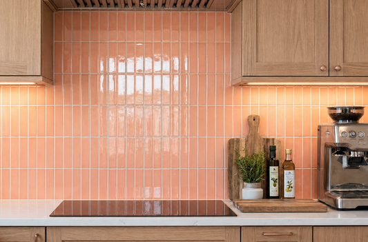 Peach glossy solid tiles by Clay Imports installed vertically as a kitchen backsplash with wooden cabinets.