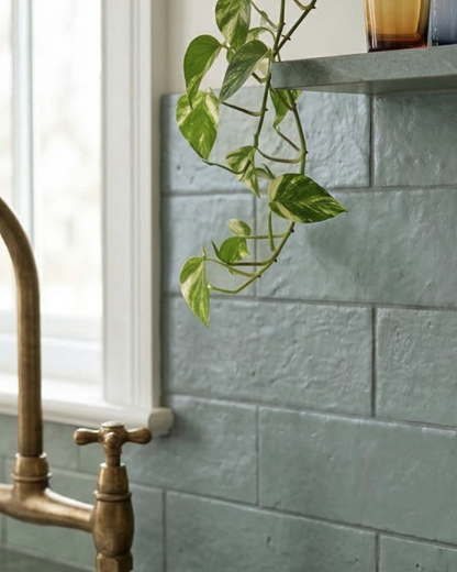 Green glazed thin brick by Clay Imports with a rough, textured finish in a subway pattern, styled with a brass faucet and a hanging plant.