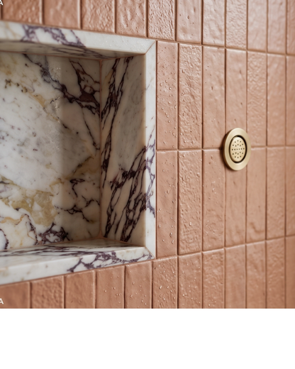 Textured Tequila Glazed Thin Brick by Clay Imports, wet with water droplets, installed alongside a veined marble shower niche and a brass shower head.