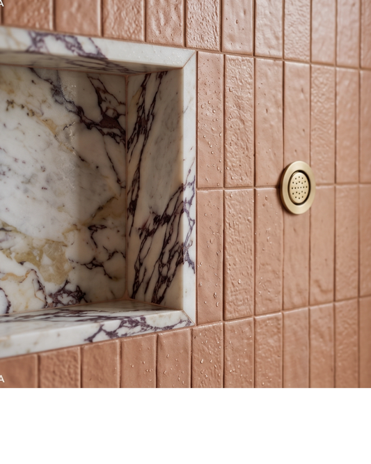 Textured Tequila Glazed Thin Brick by Clay Imports, wet with water droplets, installed alongside a veined marble shower niche and a brass shower head.