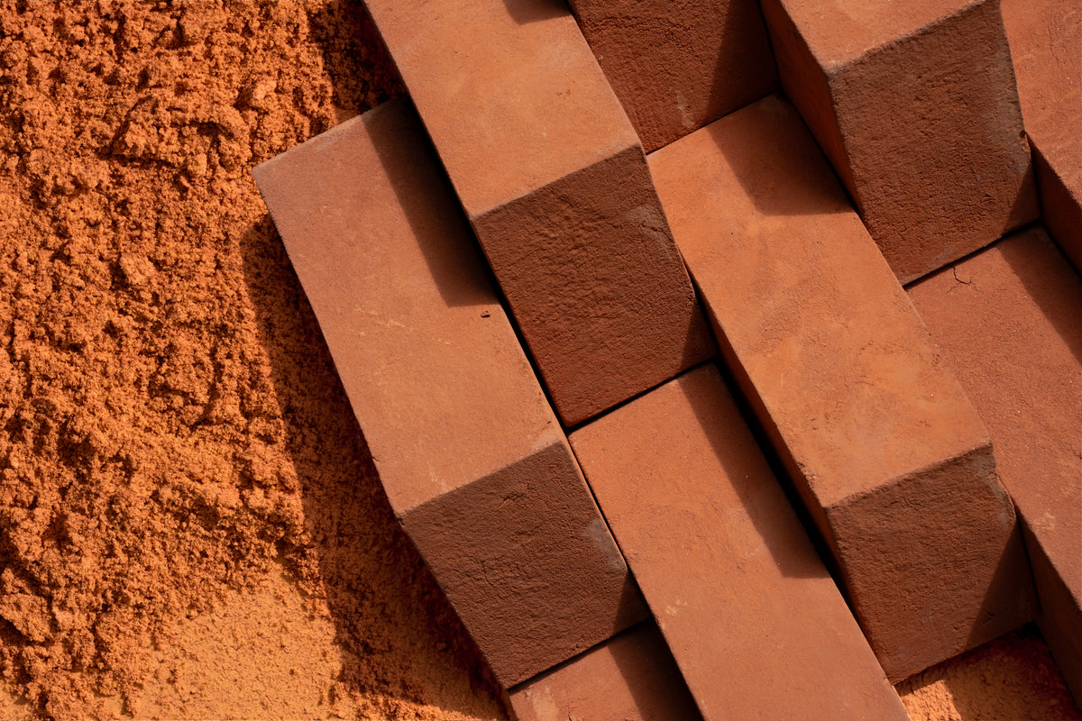 Terracotta clay bricks stacked diagonally next to a pile of fine reddish-brown soil or clay powder.