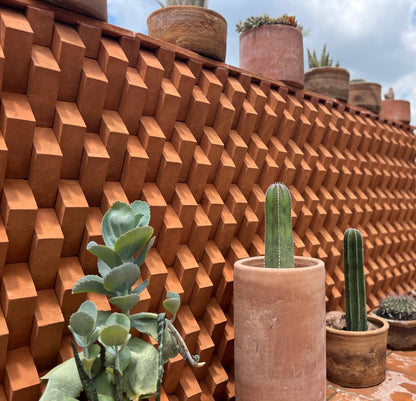 Terracotta-colored geometric textured wall panels with matching pots and cacti arranged on a tiled patio in an outdoor garden setting.