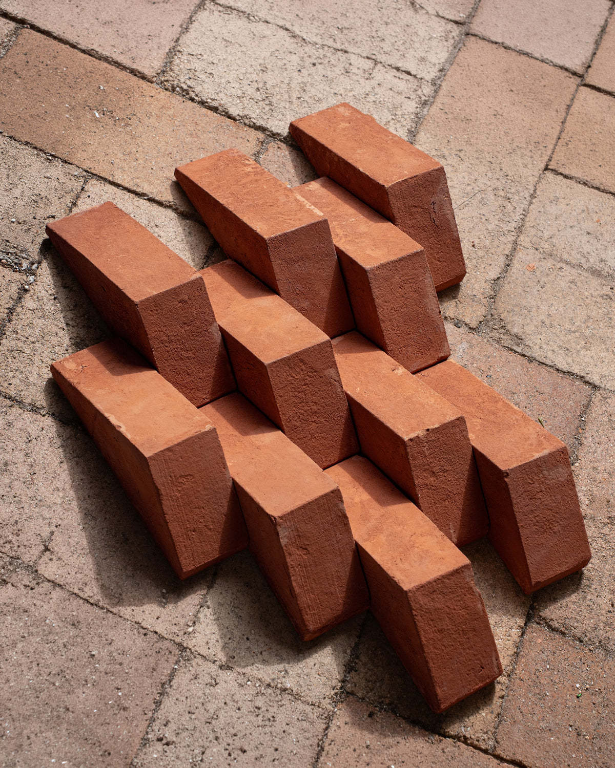 A stack of terracotta red clay bricks arranged on a paved stone surface.