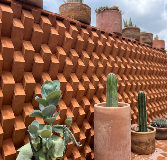 Terracotta-colored geometric textured wall panels with matching pots and cacti arranged on a tiled patio in an outdoor garden setting.