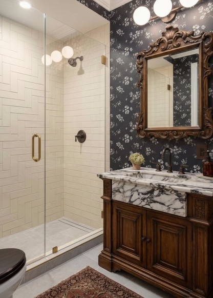 An ornate bathroom vanity with a white marble sink countertop and dark wood cabinet, set against a black floral wallpaper wall with a large carved wood mirror. A glass shower enclosure with brass hardware is visible to the left.