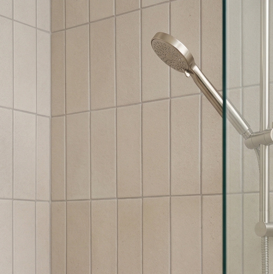 Light beige rectangular solid tile by Clay Imports, vertically laid on a shower wall with a silver shower head.