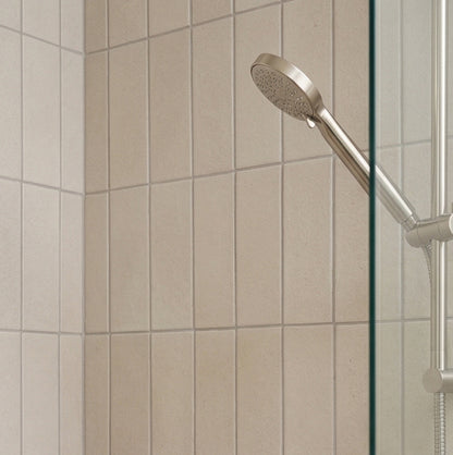 Light beige rectangular solid tile by Clay Imports, vertically laid on a shower wall with a silver shower head.