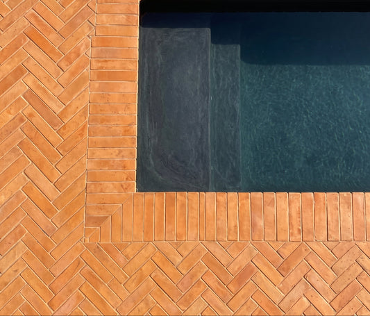 Modern architectural detail showing terracotta brick pavers arranged in a herringbone pattern framing a dark swimming pool.