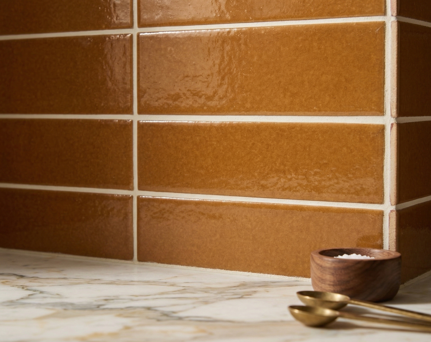 Cajeta 3x12 solid tile by Clay Imports, with a glossy, textured finish, installed on a corner wall above a marble counter, styled with a salt bowl and spoons.