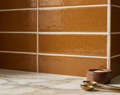Cajeta 3x12 solid tile by Clay Imports, with a glossy, textured finish, installed on a corner wall above a marble counter, styled with a salt bowl and spoons.