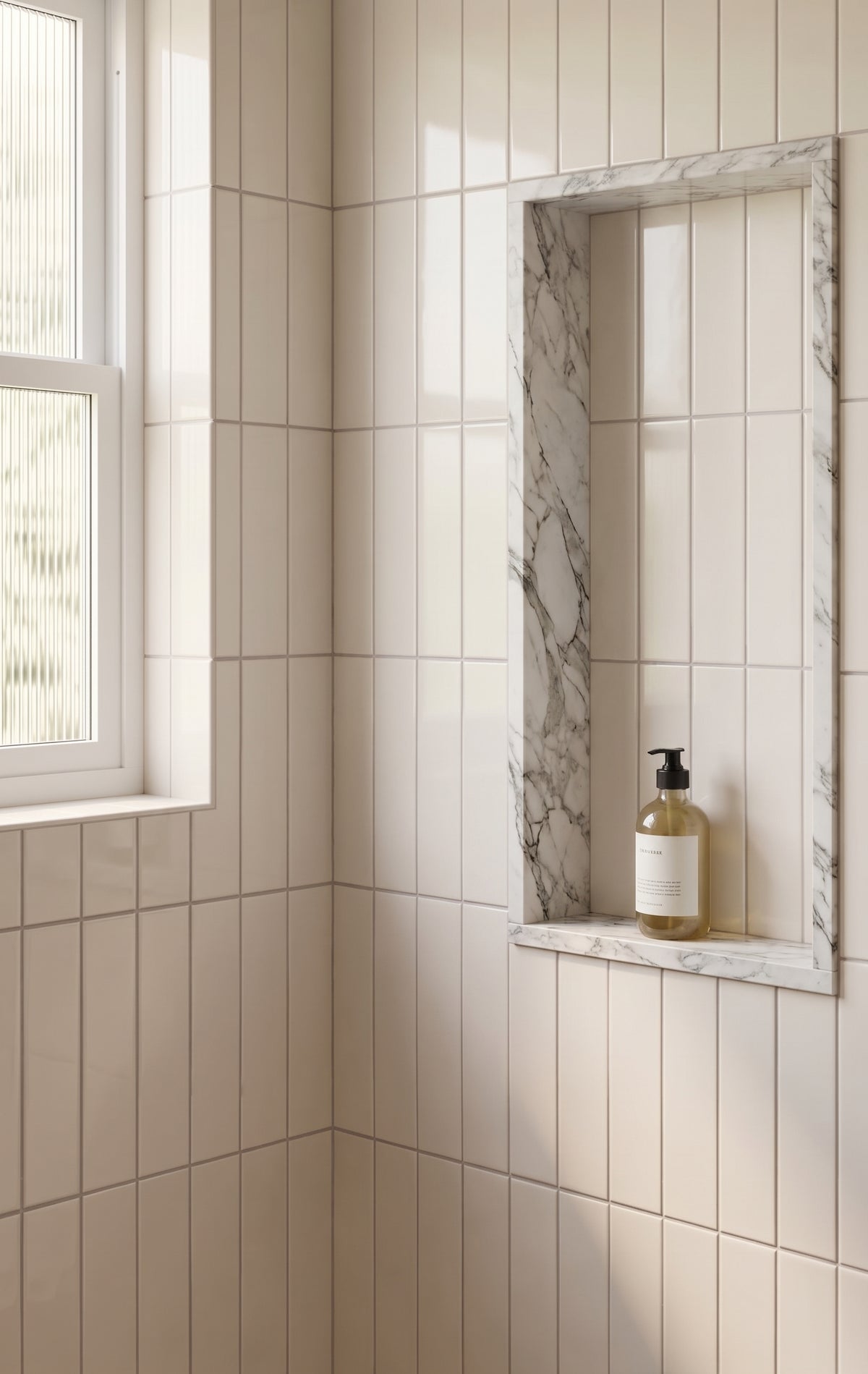 Beige subway tile bathroom wall with a recessed niche featuring a white and gray marble frame, holding a small amber bottle with a black pump.