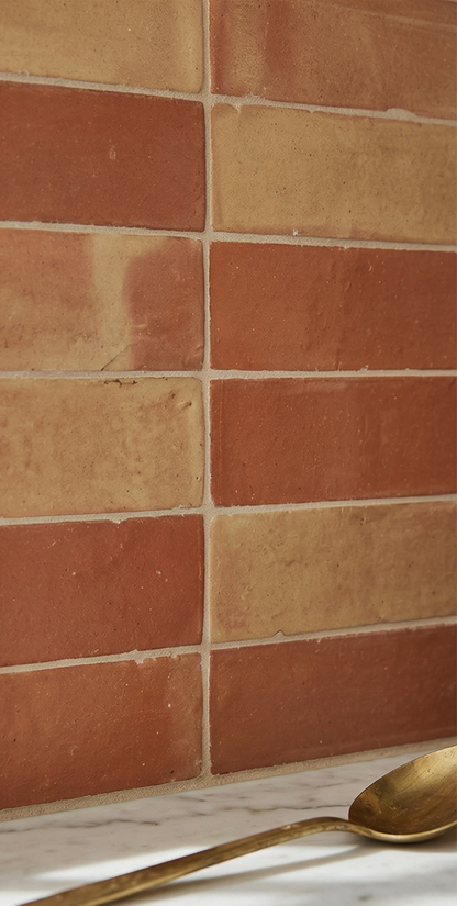 Smooth satin terracotta tiles by Clay Imports in mixed reddish-brown and beige, arranged in a staggered pattern, with a brass spoon on marble.