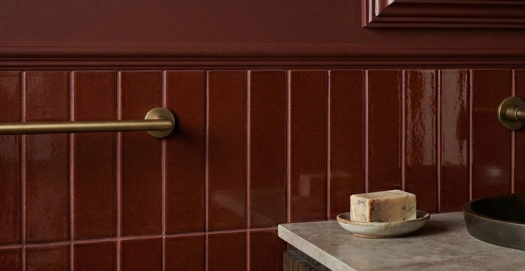Glossy reddish-brown solid tile by Clay Imports, vertically installed as wainscoting on a bathroom wall with a brass towel bar.