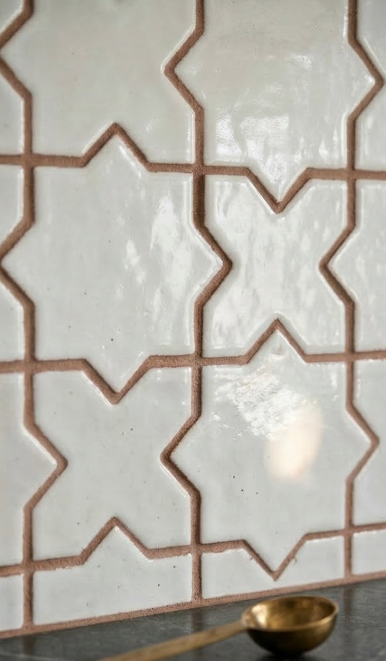 White gloss glazed terracotta tiles by Clay Imports in a mini star and cross pattern with brown grout, alongside a gold spoon.