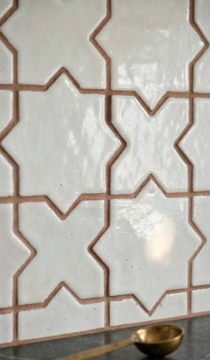 White gloss glazed terracotta tiles by Clay Imports in a mini star and cross pattern with brown grout, alongside a gold spoon.