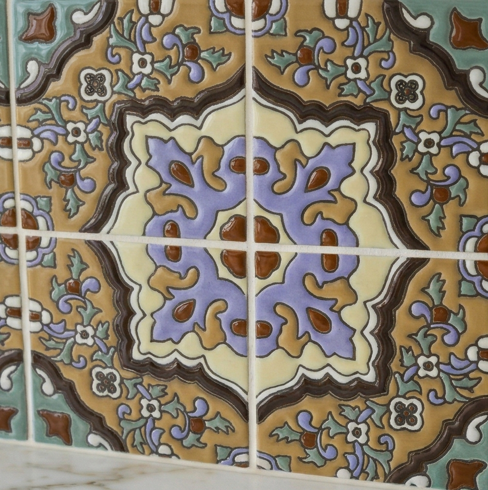 Relief Talavera tile by Clay Imports, with an intricate floral and geometric pattern in brown, gold, purple, and green.
