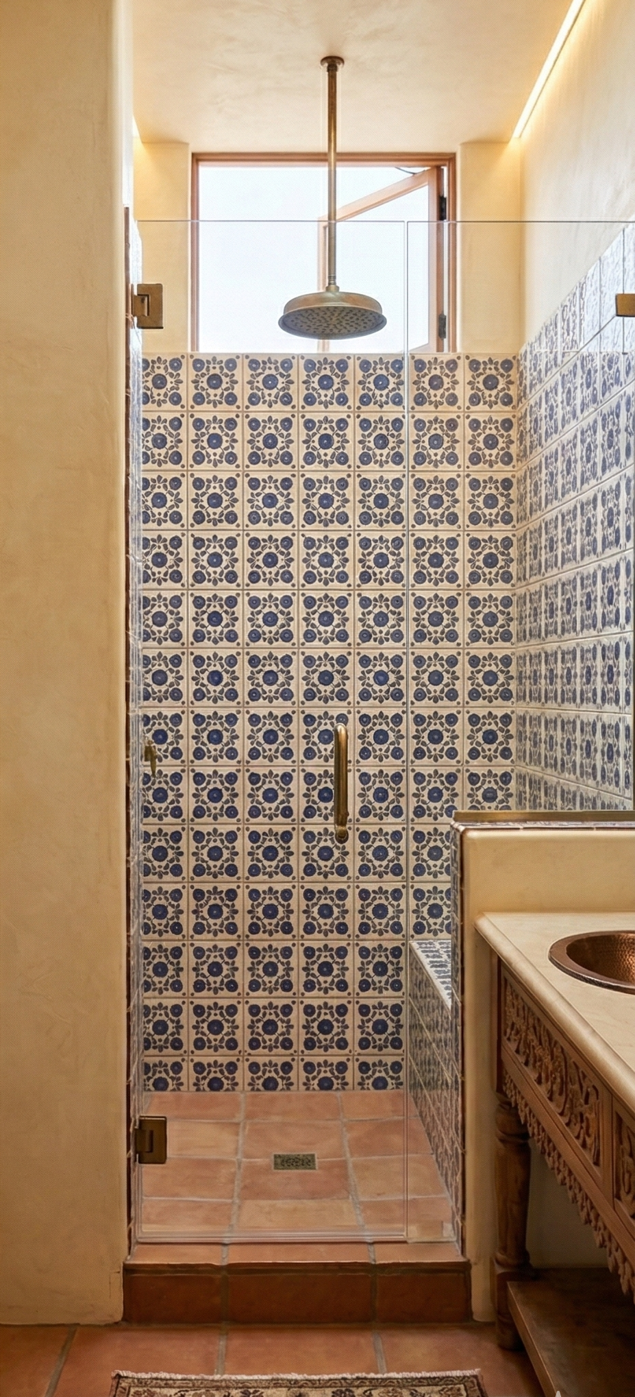 Square blue and white relief Talavera tile by Clay Imports, featuring a repeating floral motif on a shower wall with terracotta floor tiles.