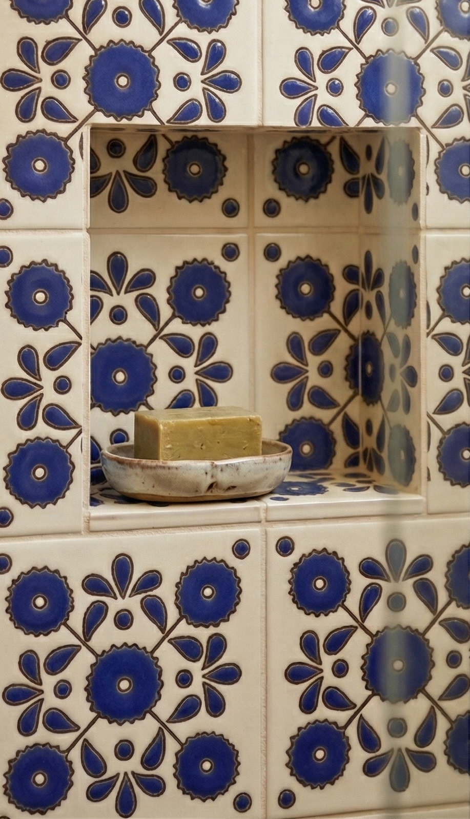 Blue and cream floral Narciso Relief Talavera tile by Clay Imports, displayed on a tiled wall with a niche holding soap.